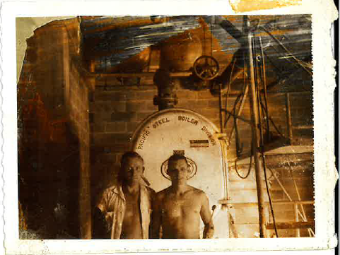 Vintage photograph of two men standing beside an industrial boiler and heating equipment.