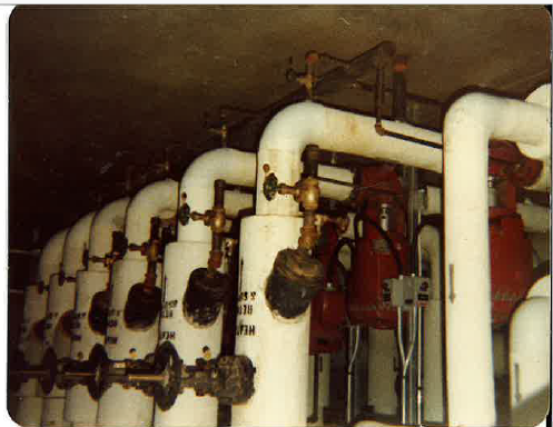 Historic industrial mechanical room with large insulated piping, valves, and interconnected equipment.
