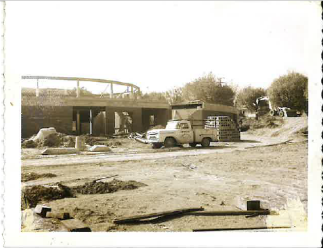 Historic construction site photograph showing a work truck beside a building under construction.