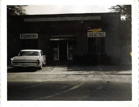 Historic plumbing and heating company storefront with a vintage car parked outside.