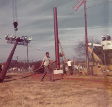 Historic photograph of workers and lifting equipment during an outdoor utility pole installation.