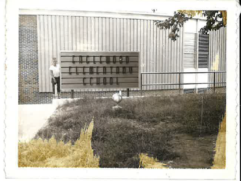 Historic photograph of a man standing beside an exterior piping installation at a commercial building.
