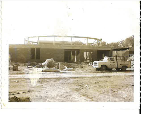 Historic construction site photograph showing a work truck beside a building under construction.